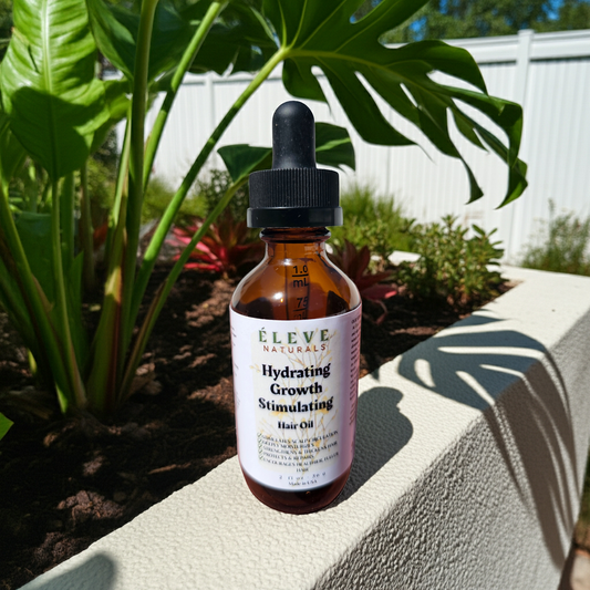 Bottle of Eleve Naturals hair oil with a dropper on a concrete surface with plants in the background